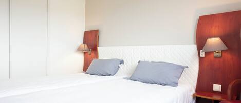 Una habitación de hotel con una cama, dos almohadas, una mesita de noche, una lámpara y una silla.