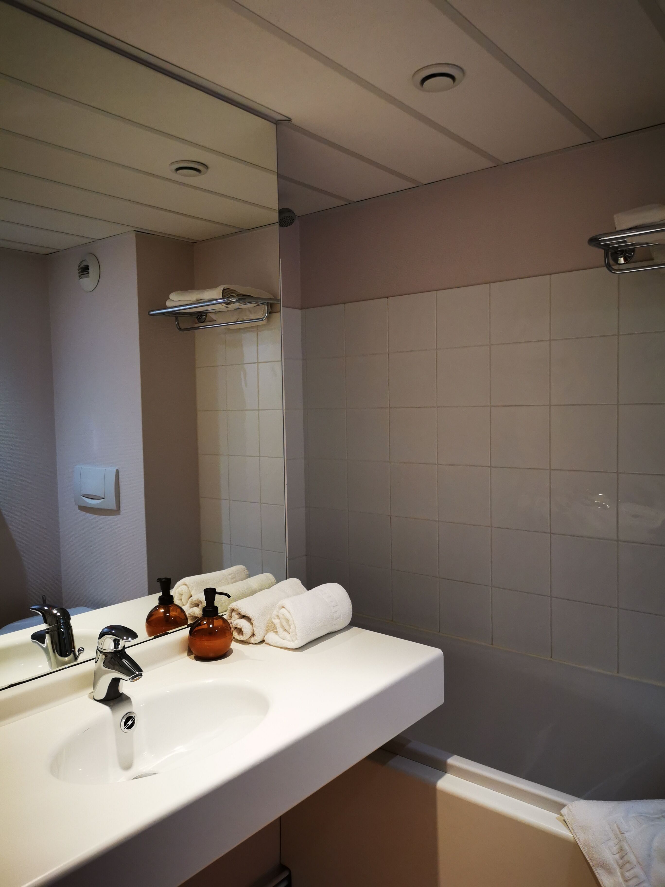 Een badkamer met een witte wasbak, een spiegel, een handdoekrek en een douchegedeelte.