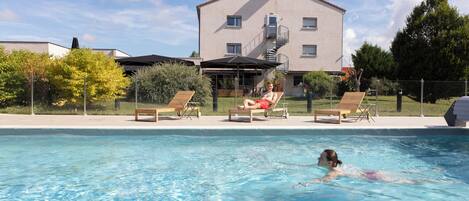 Una piscina con sillones reclinables y un edificio al fondo.