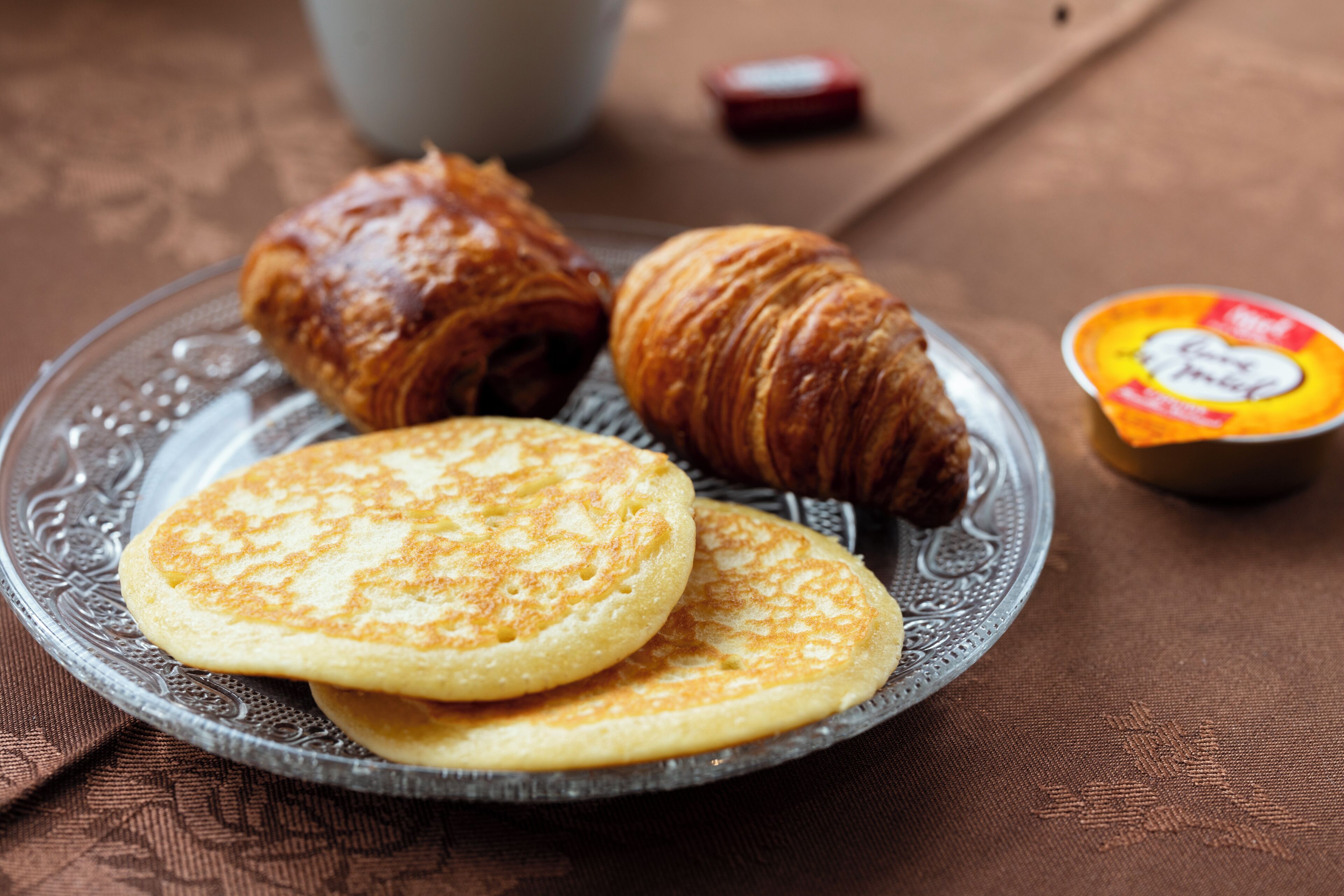 Een bord met pannenkoeken en een croissant op een glazen schotel.