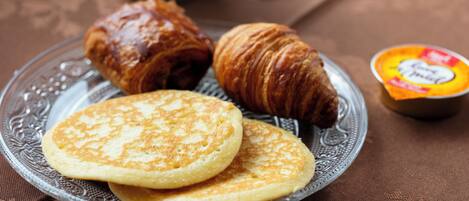 A plate with pancakes and a croissant on a glass plate.
