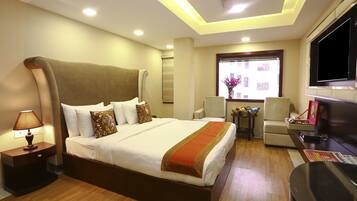 A hotel room with a large bed, a TV, a desk, and a window with a view of buildings.