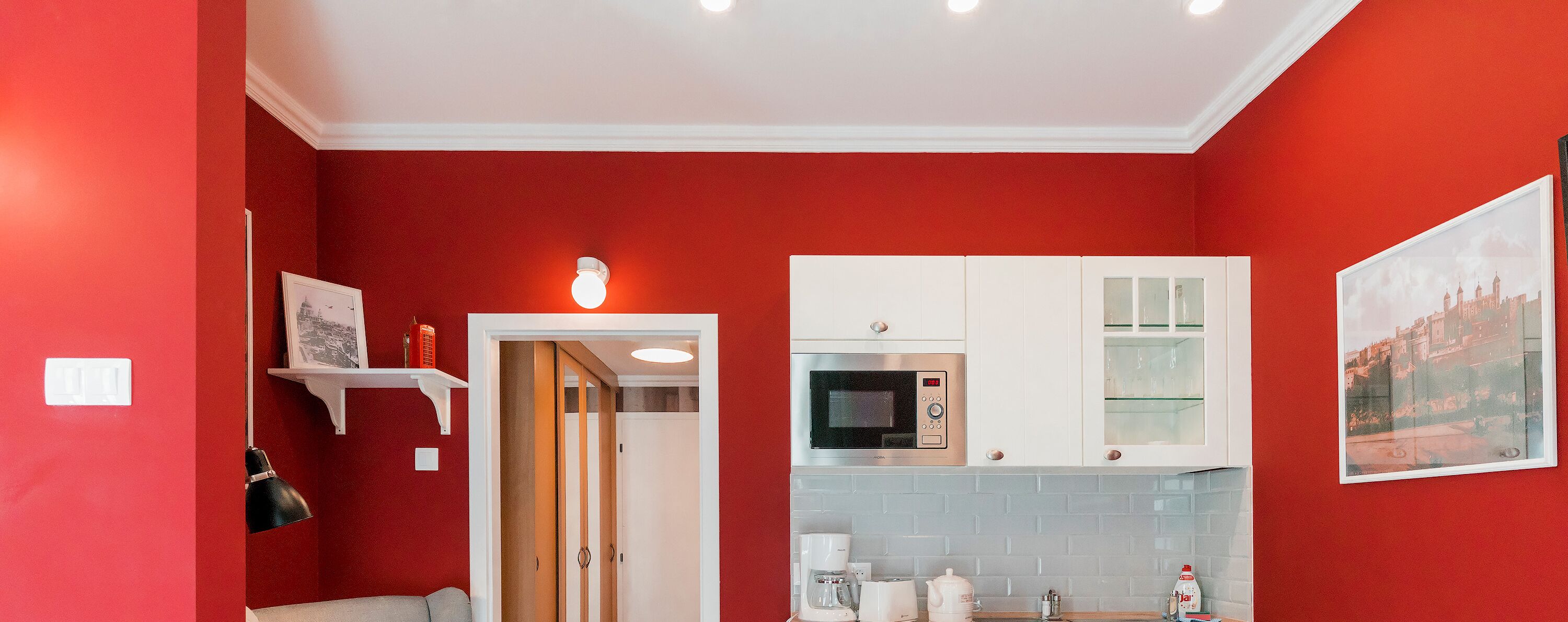 A kitchen with red walls, white cabinets, a microwave, and a coffee maker.