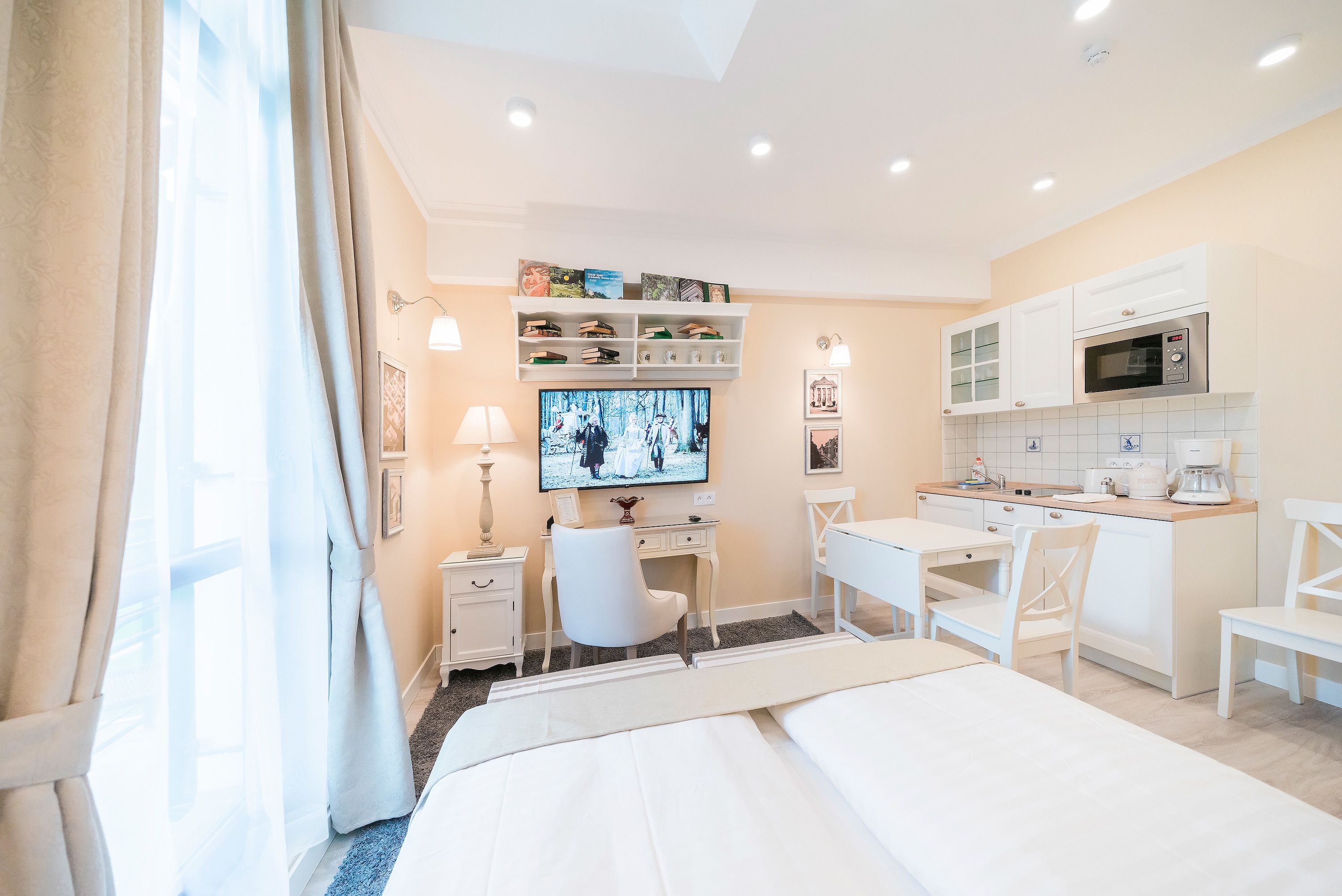 A hotel room with a bed, desk, chairs, a TV, and a kitchenette.