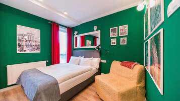 A bedroom with a bed, a chair, a mirror, and artwork on the walls.