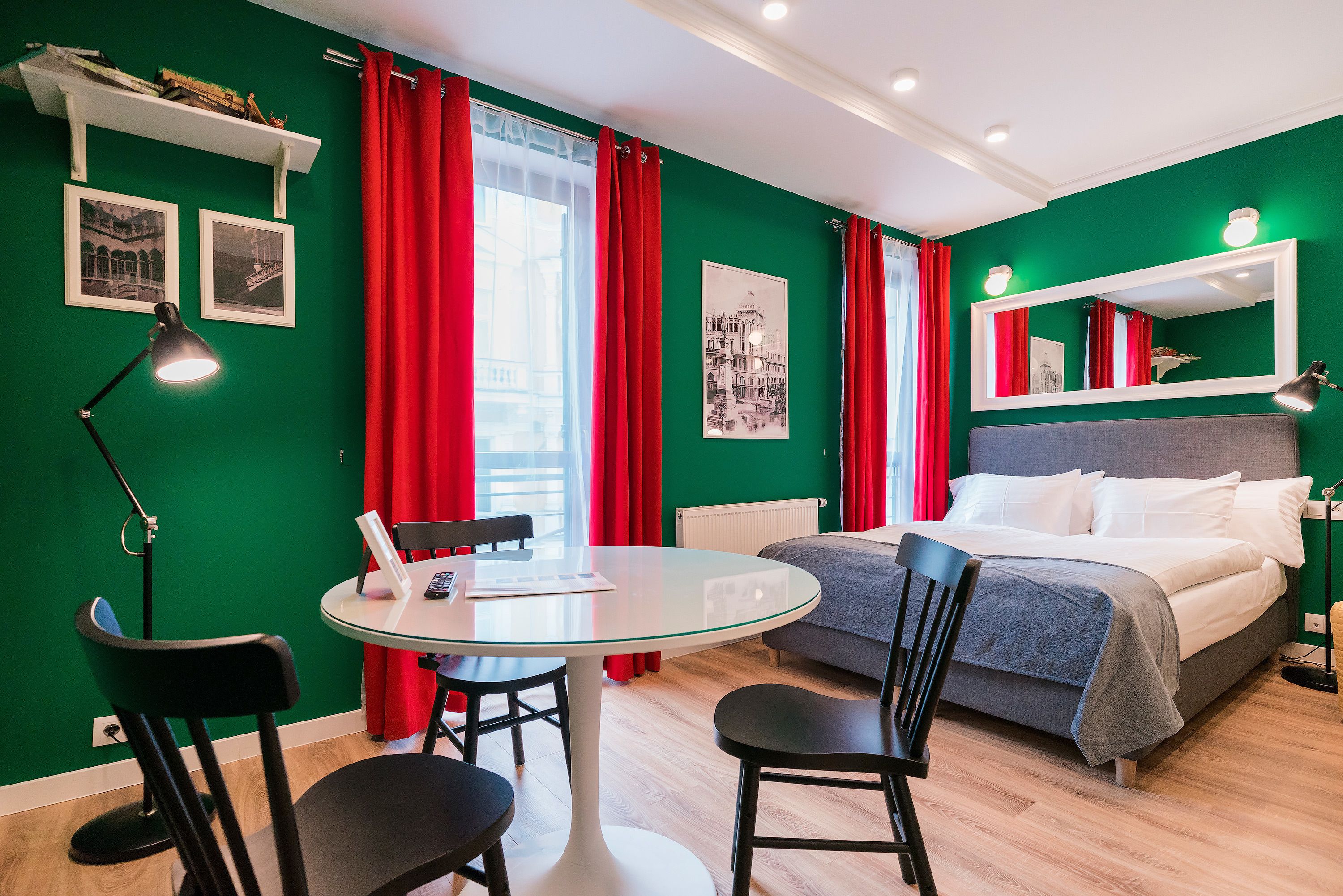 Une pièce comprenant un lit, une table ronde en verre avec des chaises, un bureau avec une lampe et des rideaux rouges.