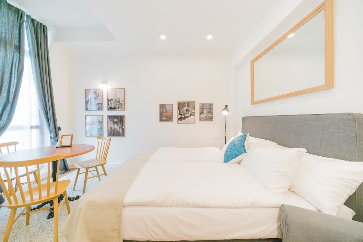 Ein Hotelzimmer mit einem großen Bett, einem Schreibtisch und Stühlen. An der Wand befinden sich gerahmte Bilder und ein großes Spiegelbild über dem Bett.