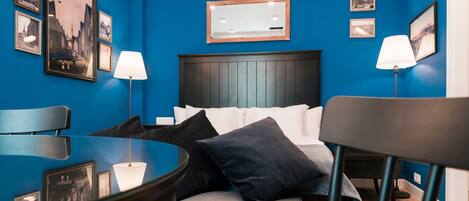 Une chambre d’hôtel avec un mur bleu, un lit avec du linge de lit blanc, deux lampes de chevet et une petite table avec une lampe.