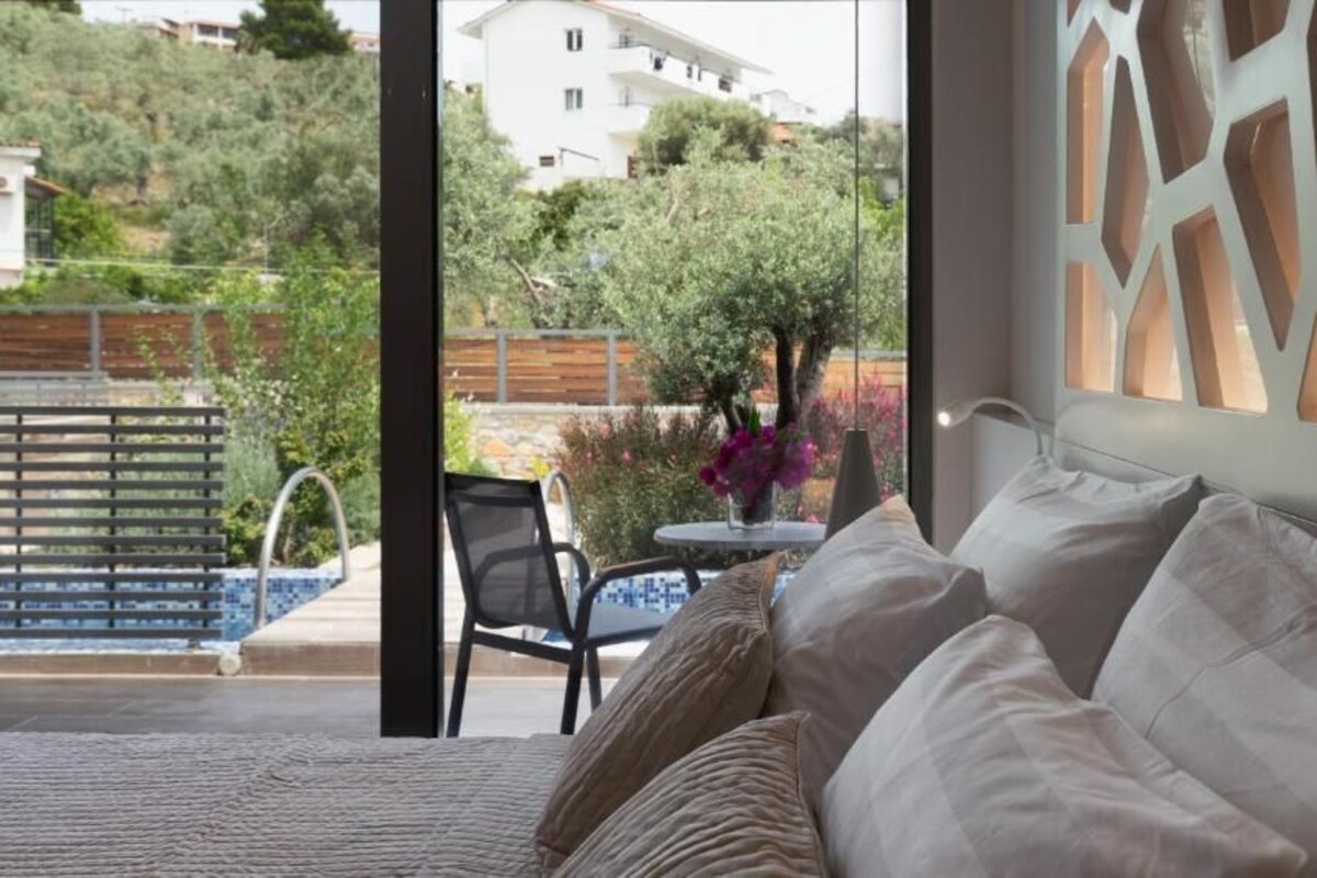 A bedroom with a bed, a chair, a table, and a view of a pool and greenery outside.
