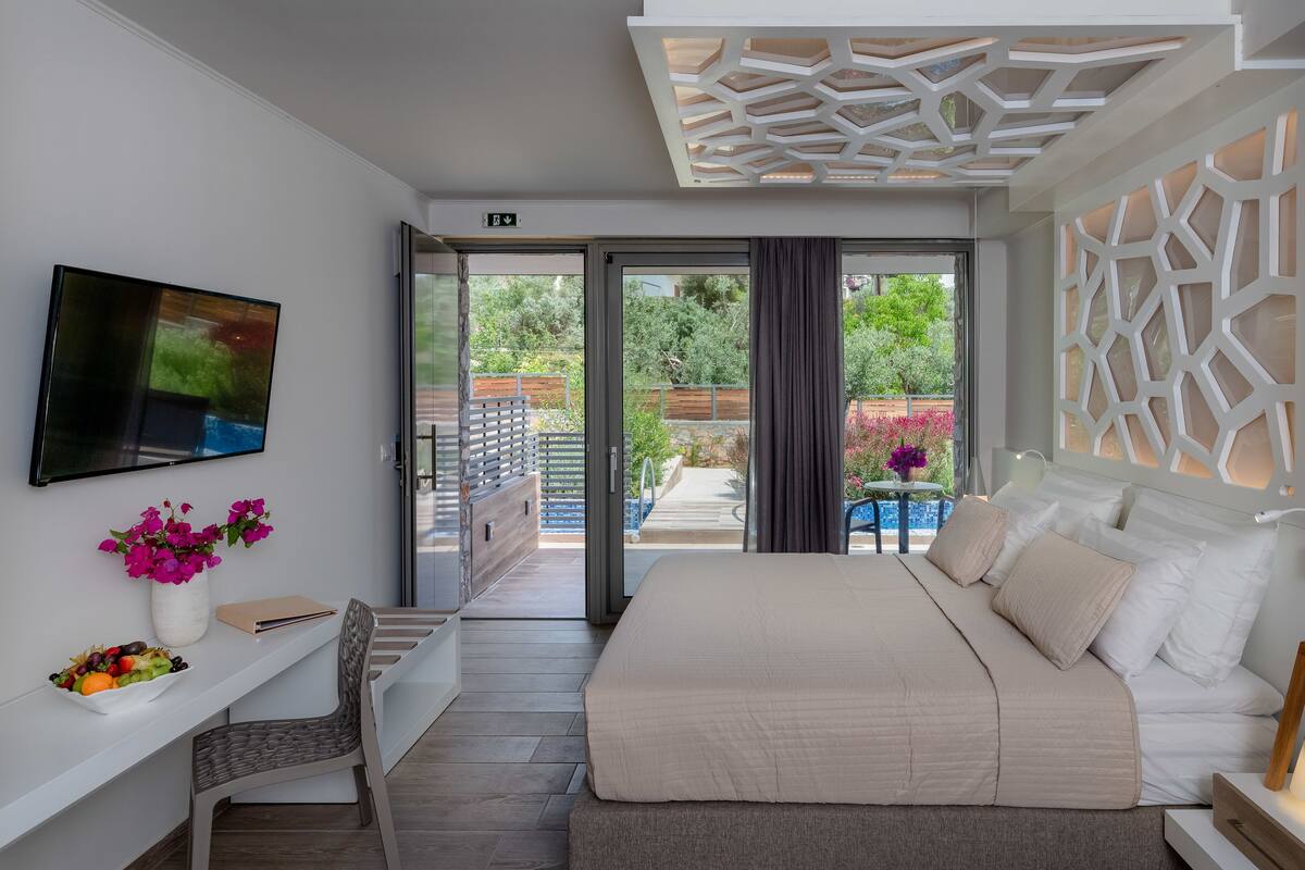 A modern bedroom with a bed, a TV, a desk, and a view of the garden.