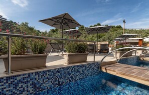 A pool area with tiled flooring, lounge chairs, and umbrellas. - KB Ammos (Skiathos)
