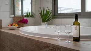 A bathroom with a bathtub, a bowl of fruit, a bottle of wine, and two wine glasses on the counter. - KB Ammos (Skiathos)