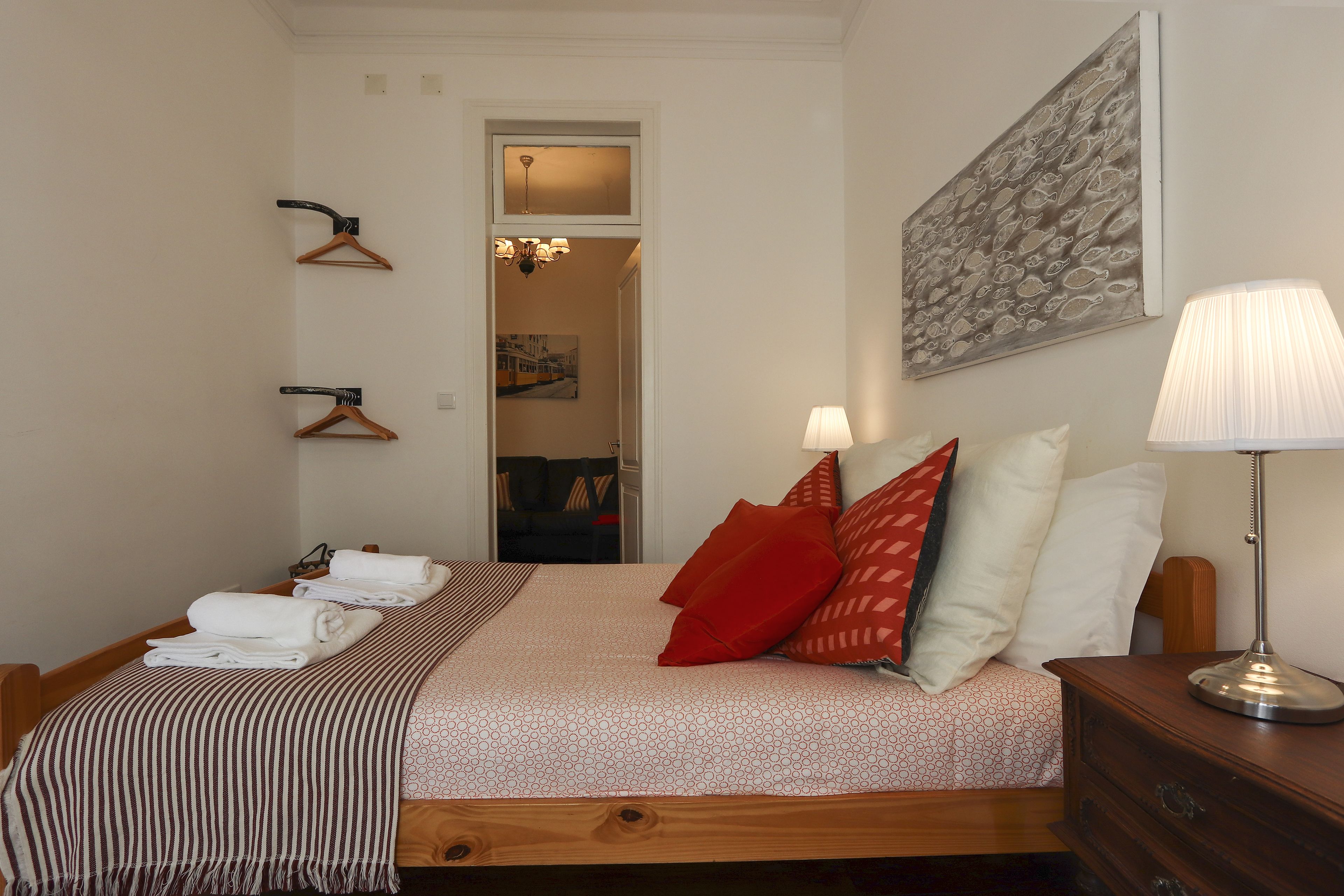 Una cama bien hecha con una manta a rayas, una lámpara de noche y una mesita de madera.