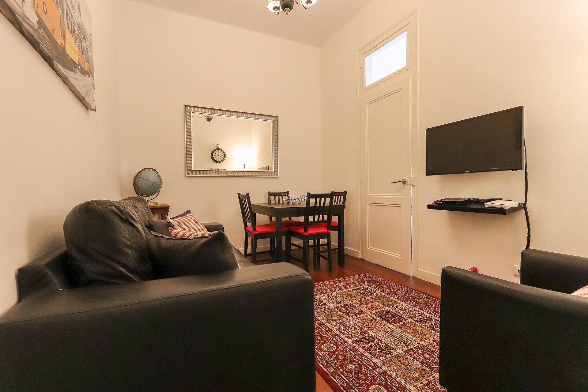 A living room with a sofa, a dining table with chairs, a TV mounted on the wall, and a globe on a side table.