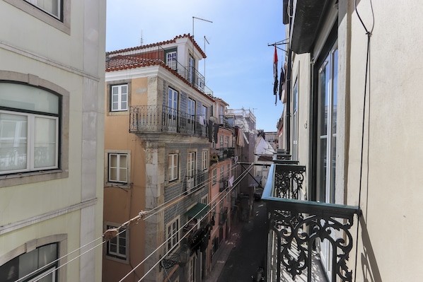 Une rue étroite, bordée de bâtiments des deux côtés, avec des balcons dotés de balustrades et des fenêtres.