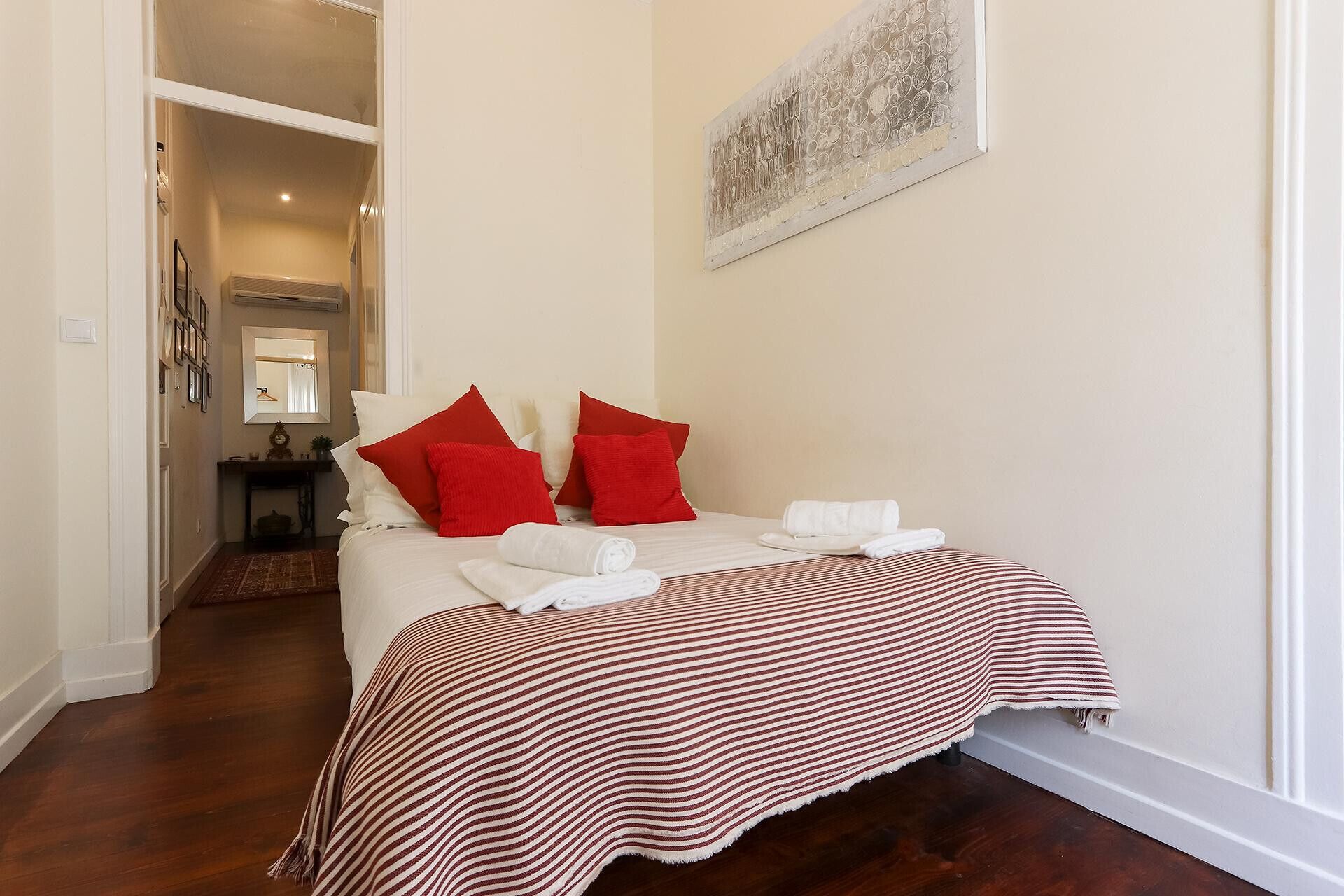 A neatly made bed with red and white bedding, a striped blanket, and white towels.