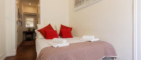 A neatly made bed with red and white bedding, a striped blanket, and white towels.