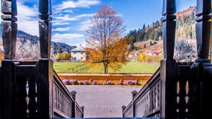 Une vue depuis un balcon doté d’une balustrade en bois, donnant sur une zone herbeuse avec un arbre et un bâtiment en arrière-plan.