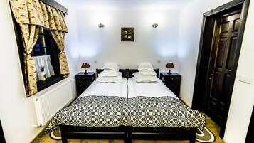 A double bed with a patterned bedspread, two bedside tables with lamps, a window with curtains, and a door.