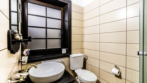 A bathroom with a large window, a sink, a toilet, and a shelf with toiletries.