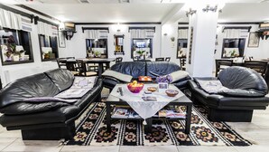 Un salon avec deux canapés en cuir noir, une table basse avec des magazines, un tapis à motifs et, au fond, un coin repas.