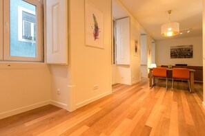 Une pièce spacieuse avec un plancher en bois, des murs blancs et un coin repas doté de chaises orange.
