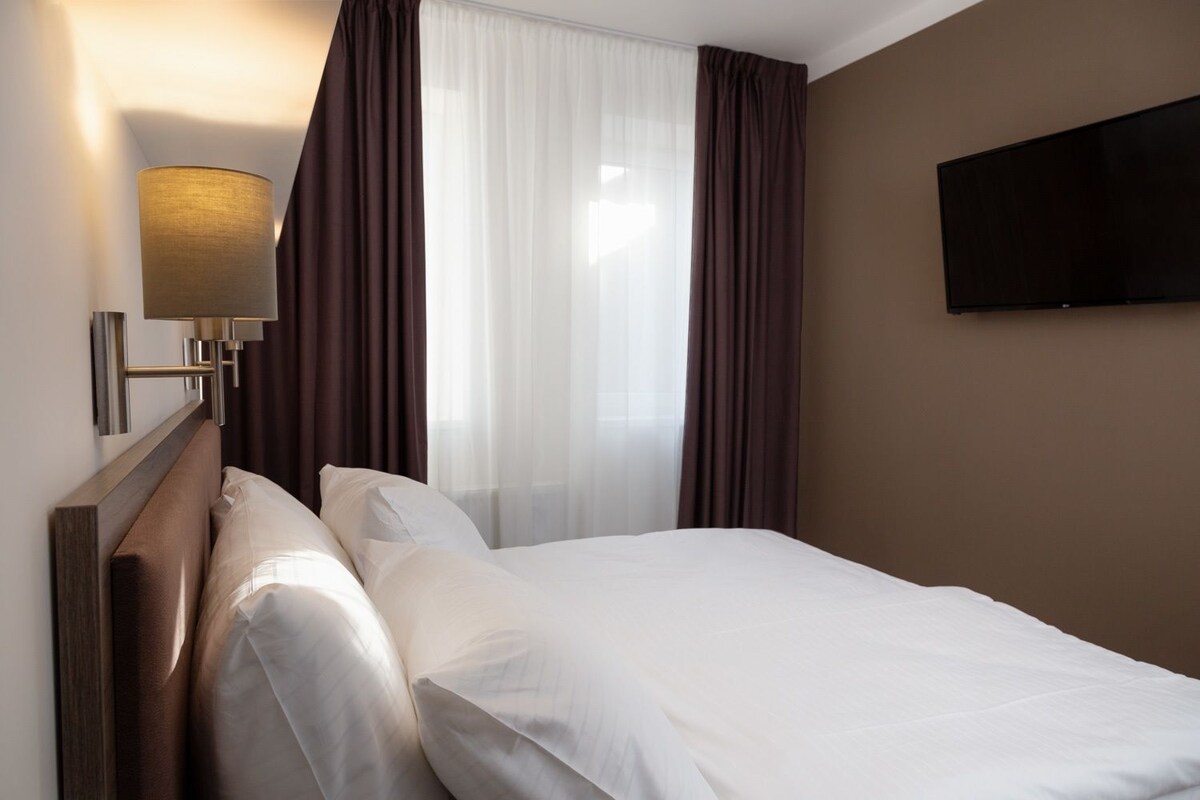Una habitación de hotel con una cama, un televisor montado en la pared y una lámpara.