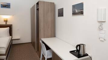 A hotel room with a bed, a desk, a chair, a kettle, and a phone.