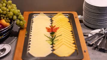 Una mesa de buffet con queso en rodajas, frutas y verduras.