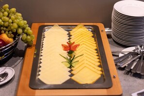Buffet com queijo fatiado, frutas e legumes.