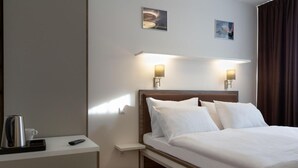 A hotel room with a bed, bedside lamps, a nightstand, a remote control, and a coffee maker. - SKY Hotel Prague (Prague)