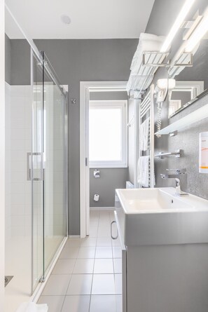 A modern bathroom with a glass shower enclosure, a large sink, and a mirror with integrated towel racks. - SKY Hotel Prague (Prague)