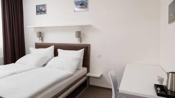 A hotel room with a double bed, a desk, and two wall-mounted lamps.