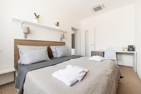 Una habitación de hotel con una cama, mesitas de noche, un escritorio y un espejo.