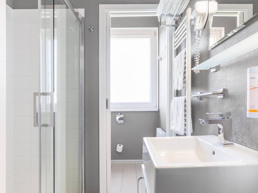Un baño moderno con cabina de ducha de vidrio, un lavamanos espacioso y un espejo con toalleros integrados.