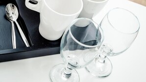 A tray with a stainless steel kettle, white cups, a glass, and a spoon. - SKY Hotel Prague (Prague)