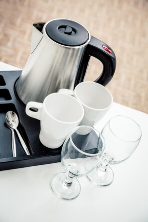 Una bandeja con un hervidor de acero inoxidable, tazas blancas, un vaso y una cuchara.