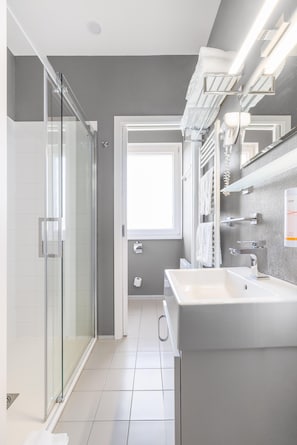 Un baño moderno con cabina de ducha de vidrio, un lavamanos espacioso y un espejo con toalleros integrados.