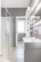 Un bagno moderno con cabina doccia in vetro, un lavandino capiente e uno specchio con portasci integrati.