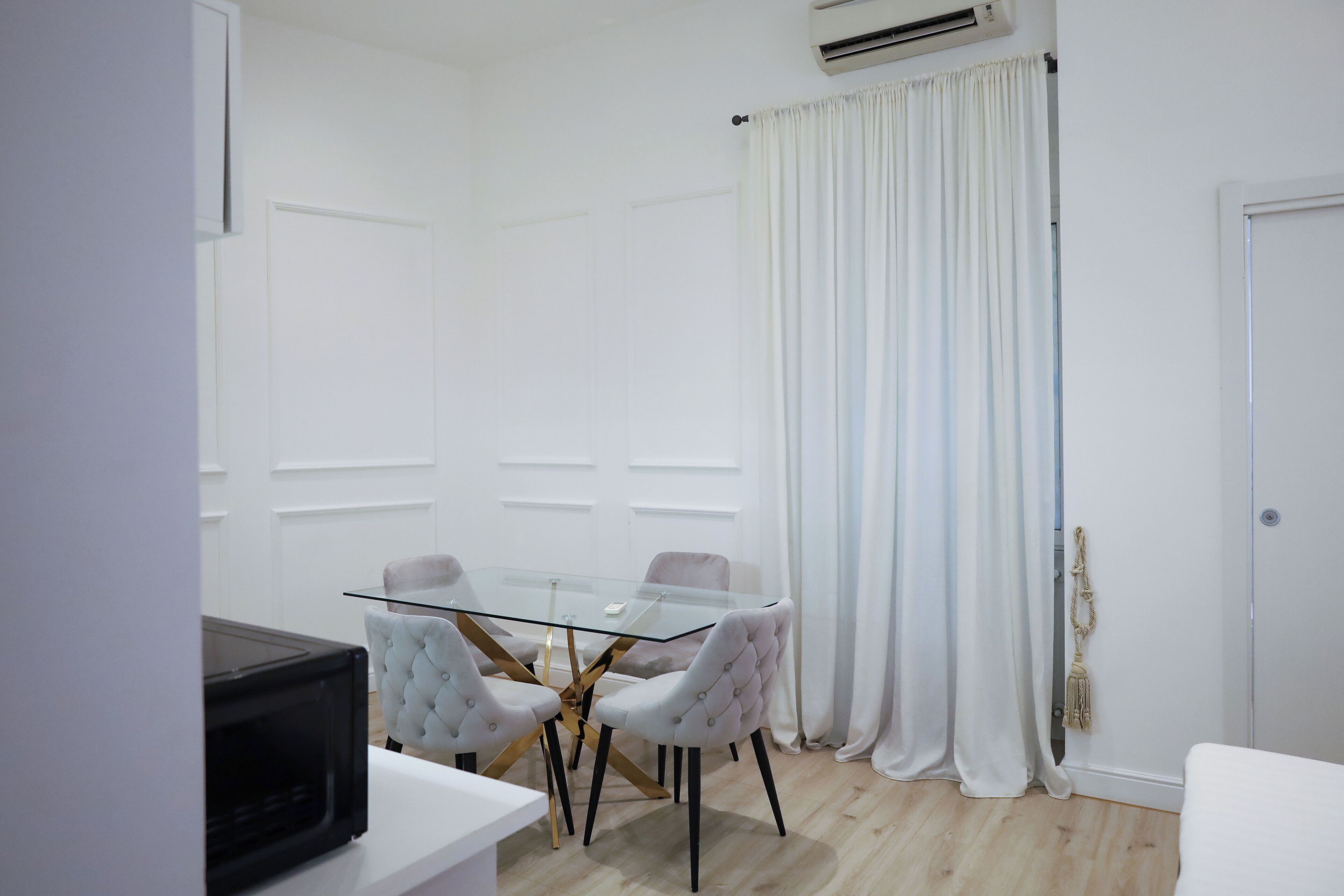 A modern dining area with a glass table and tufted chairs, white walls, and a white door.