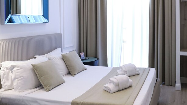 Moderni hotellihuone, jossa on suuri sänky, yöpöytä, peili ja näkymä ulos.