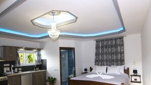 A modern bedroom with a large bed, a chandelier, a shower room, and a kitchen area. - Villa Olive Tree (Kissamos)