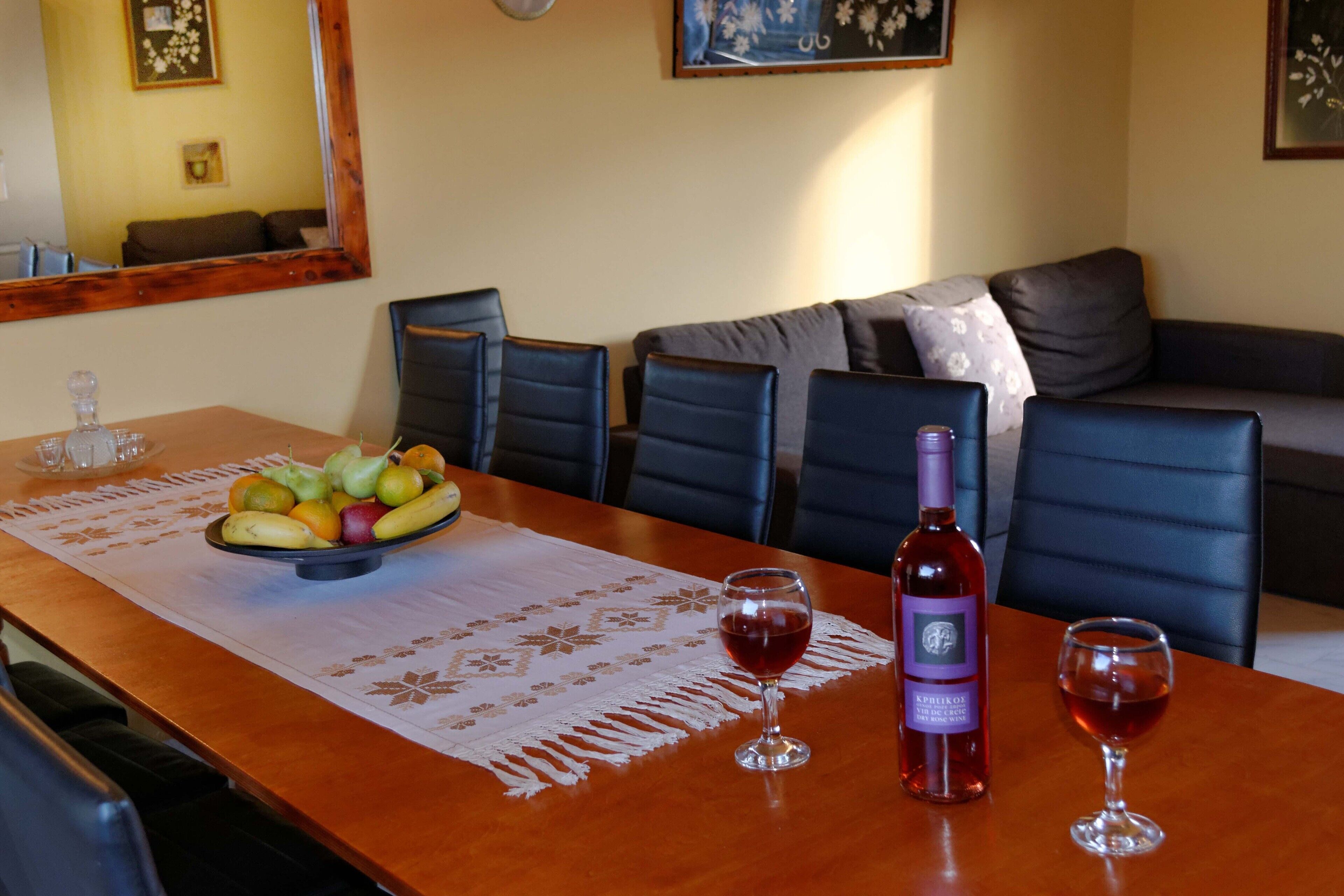 A dining table with a fruit bowl, two wine glasses, and a wine bottle.