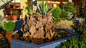 A rock garden with potted plants and a wooden chair. - Villa Olive Tree (Kissamos)