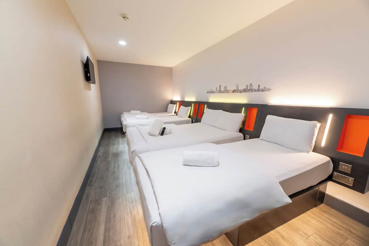 A hotel room with three single beds, each with a white bedspread and pillows, and a small bedside table.