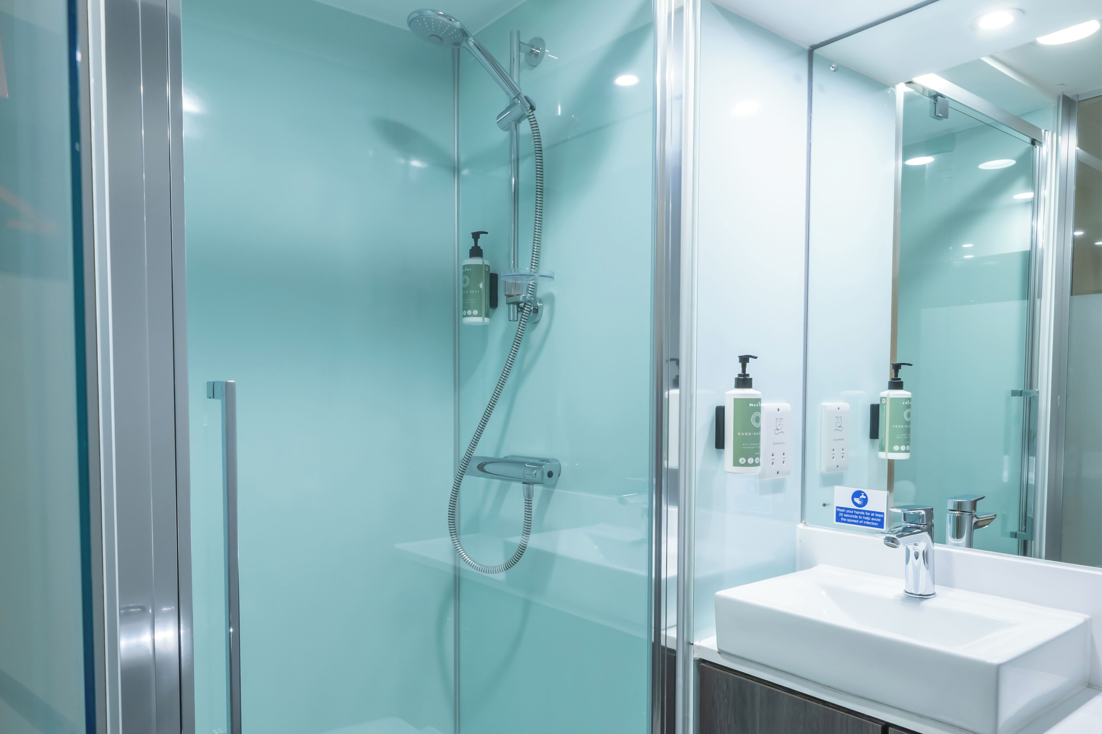 A modern bathroom with a glass shower enclosure, a white sink, and a mirror.