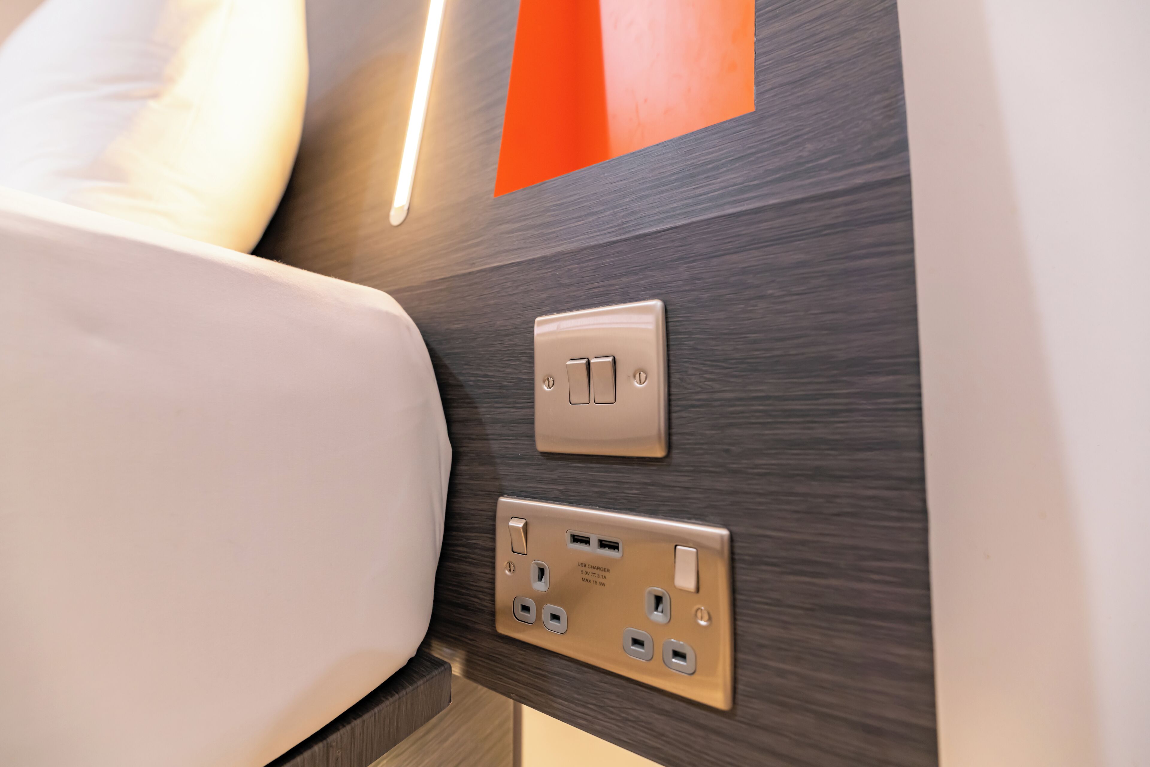 A modern bathroom with a wooden wall, a white bathtub, and a wall-mounted light fixture.