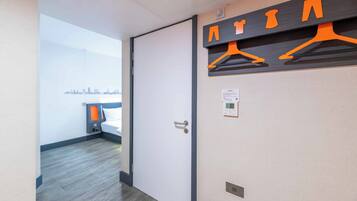 A hotel room with a city skyline view, a door, a coat rack with hangers, and a thermostat on the wall.