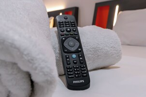A black Philips remote control on a white bed with a white fluffy pillow.