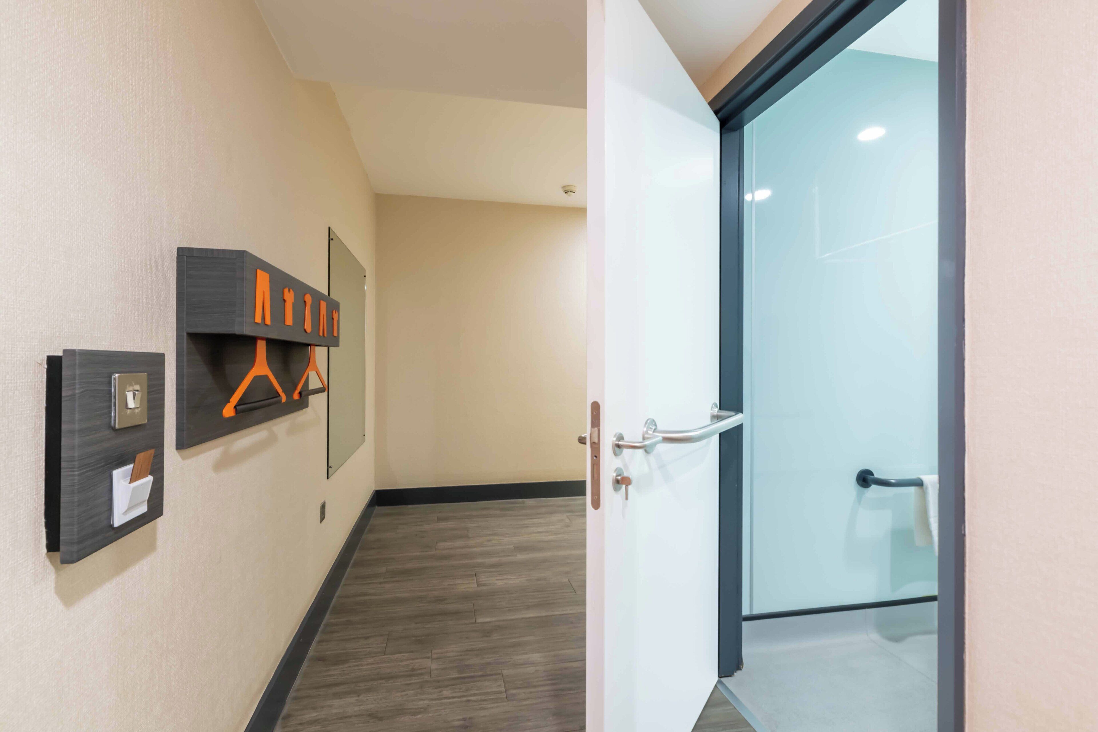 Un pasillo con una puerta que da a un baño, un interruptor de luz en la pared y un perchero.
